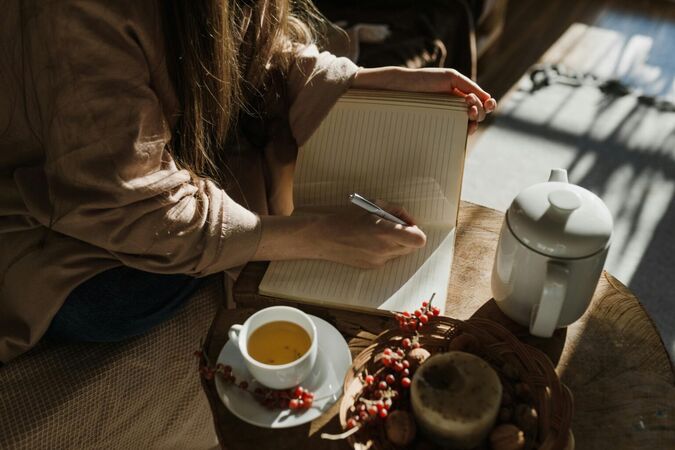Frau beim Tee am Schreibtisch in den Appartements Das Edelweiss in Grän, Tannheimer Tal, Tirol, schreibt in ein Notizbuch.