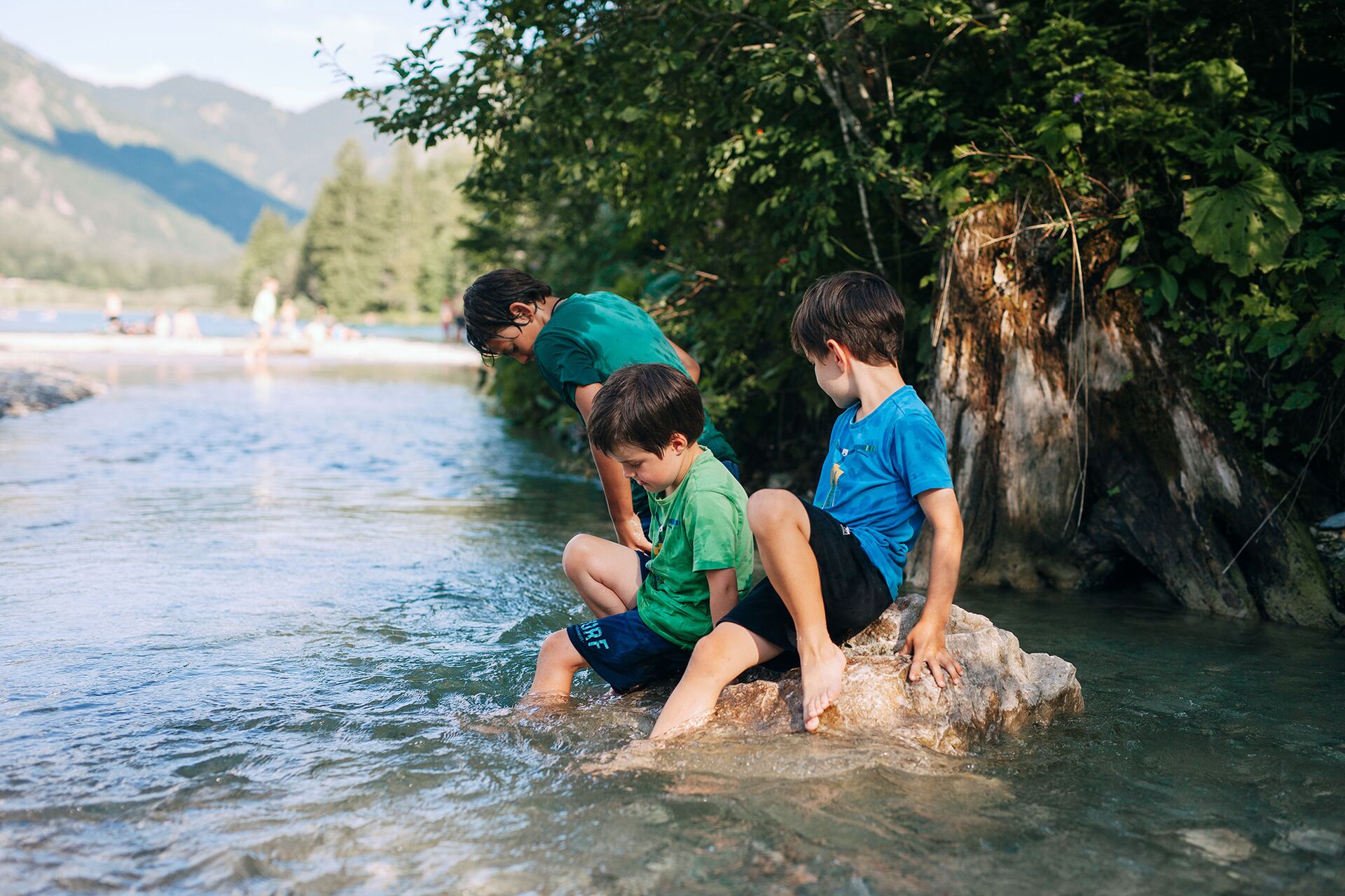 Ein Kind steht im Wasser des Haldensees, zwei weitere Kinder sitzen auf einem Stein mit den Füßen im See.